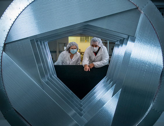 Two people wearing protective clothing observe the inside of a tracker plane during production.